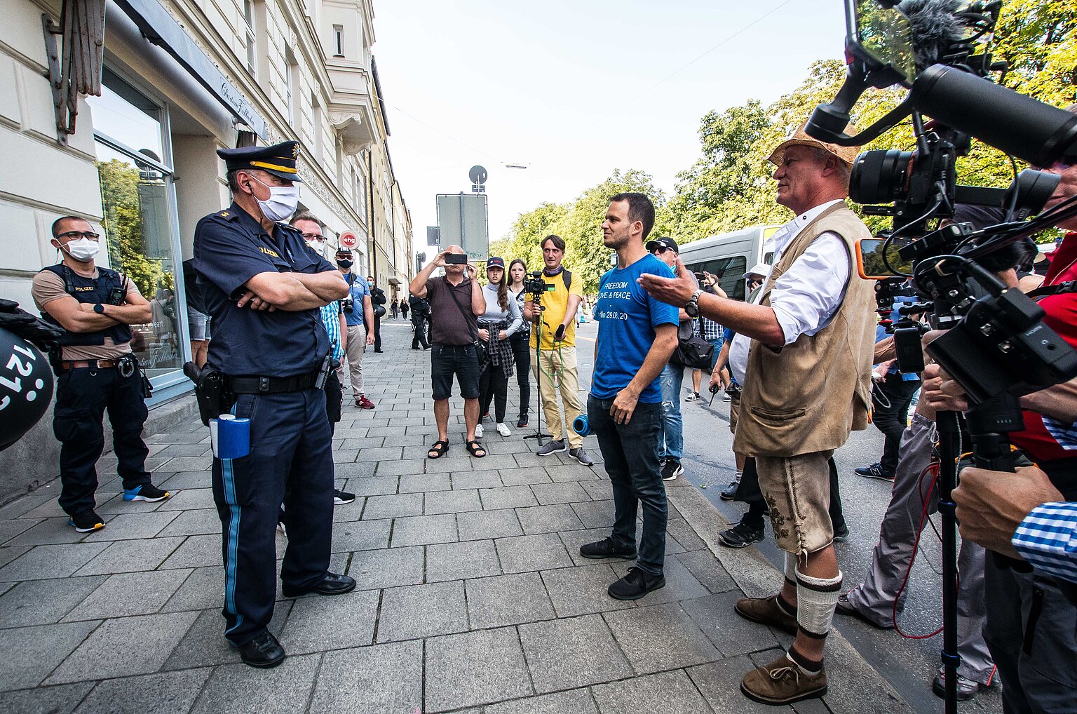 Zwei Männer diskutieren bei einer Querdenker-Demonstration mit einem Polizisten – Von rechts: Der ehemalige Polizist und Coronaleugner Karl Hilz und Markus Haintz (blaues T-Shirt), Rechtsanwalt einiger Querdenken-Initiativen, streiten im März in München mit einem Polizisten