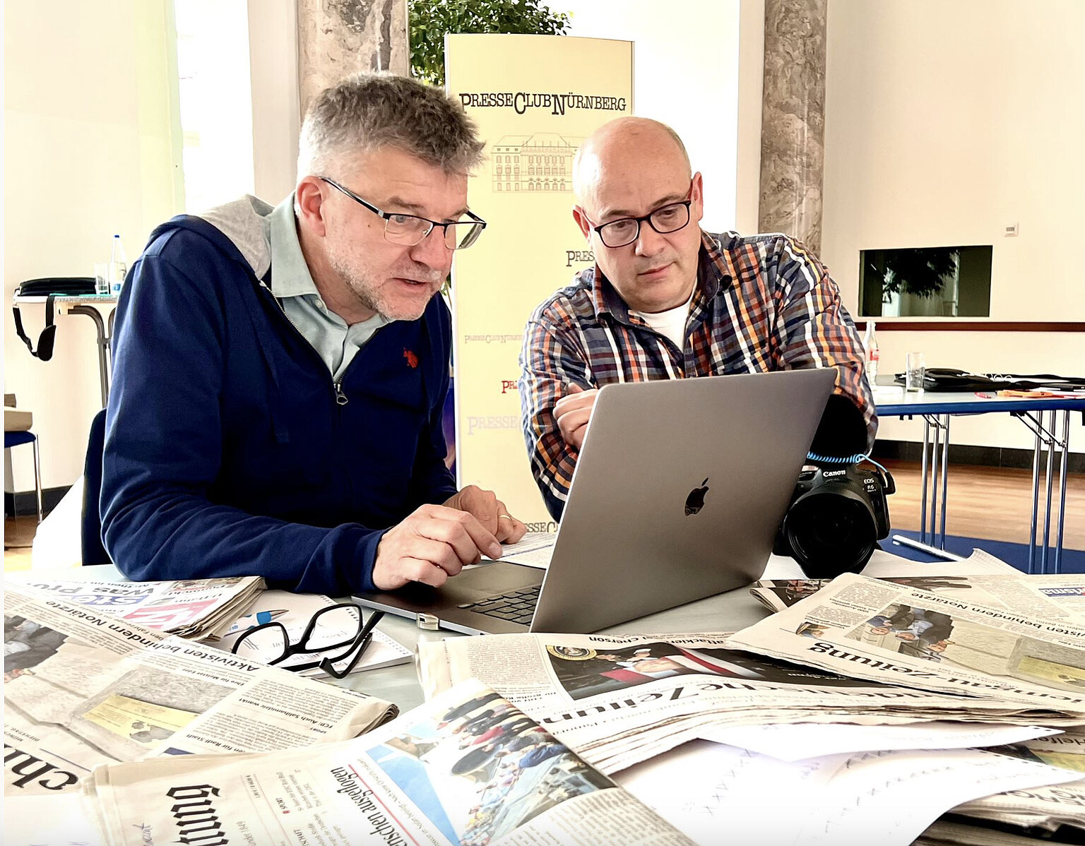 Zwei Männer sitzen an einem Laptop-Bildschirm, auf dem Schreibtisch liegen einige Zeitungen – Ferdinand Dörfler-Farthofer (rechts) und Thomas Geiger prüften mehr als 2400 Fotovermerke in 25 bayerischen Tageszeitungen