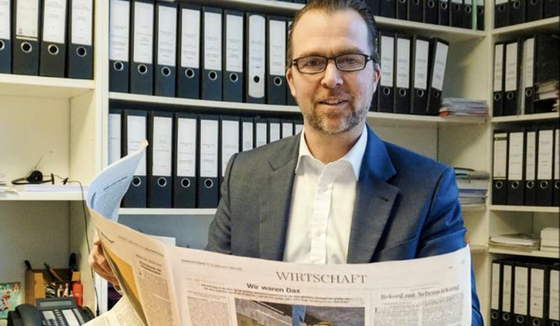 Lächelnder Mann, der in einem Büro den Wirtschaftsteil der Süddeutschen Zeitung liest – „Beeindruckende Entscheidung für die Pressefreiheit“: Rechtsanwalt Martin Schippan