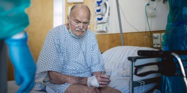 Älterer Patient sitzt auf seinem Krankenhausbett